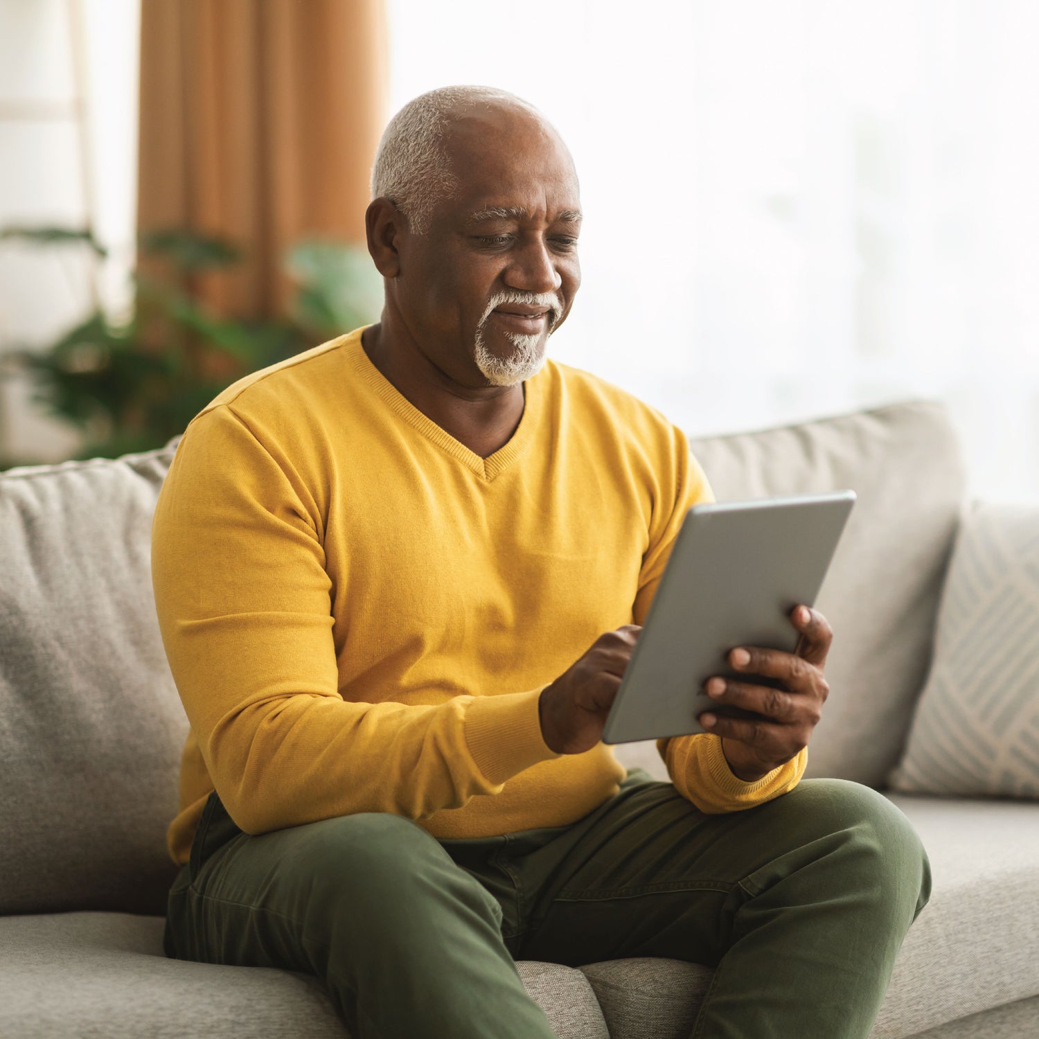 Older man smiling while using an iPad at home